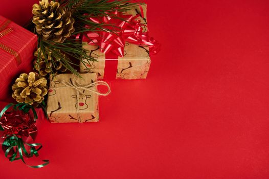 Christmas still life with gift boxed and golden pine cones in the corner of a red background with copy ad space for text. Mockup with cute presents, decorated with wrapping paper and satin shiny bows