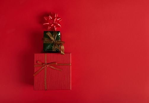 Flat lay. Horizontal studio shot of stylish gift boxes wrapped in red and green wrapping paper, laid out in the shape of a Christmas tree, decorated with bow on red background. Copy space. Still Life