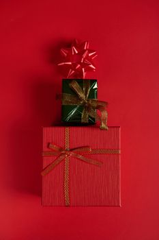 Flat lay. Vertical studio shot of cute stylish gift boxes, laid out in the shape of a Christmas tree, decorated with bow on red background. Still life. New Year's event. Boxing Day. December 25. Xmas