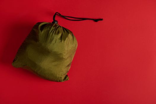 Still life with shiny khaki satin bag with Christmas gifts inside on red background. Copy ad space. Top view of a green bag, isolated on colored background with space for promotional text. Boxing Day