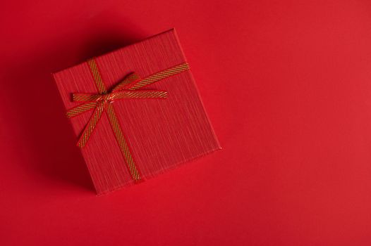 Top view, cute romantic present in stylish red gift box for Christmas, New Year, Saint Valentine's or Women's Day on red background. Copy advertising space. Boxing Day. Packing gifts for any event