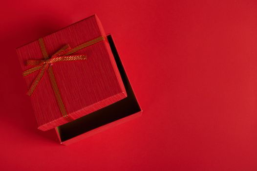 Monochrome still life with an open stylish red gift box with tied bow on red background with copy advertising space. Top view of romantic surprise for Christmas, Saint Valentine's or Women's Day