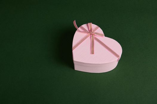 Top view. Romantic present, a heart shaped pink gift box with a cute surprise for Saint Valentine's or Women's Day, isolated on a green backdrop with copy advertising space. February 14, March 08