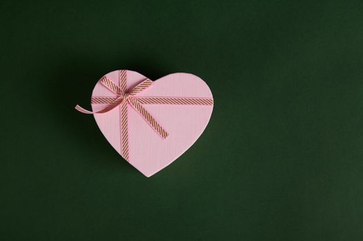Flat lay composition with a heart shaped pink gift box with ribbon tied bow, isolated on green background with copy ad space. Cute romantic present for Saint Valentine's Day, International women's Day