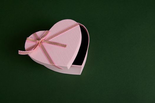 View from above to a still life with an open romantic present, a heart shaped pink gift box with a surprise inside, for Saint Valentine's or Women's Day, on green backdrop with copy advertising space