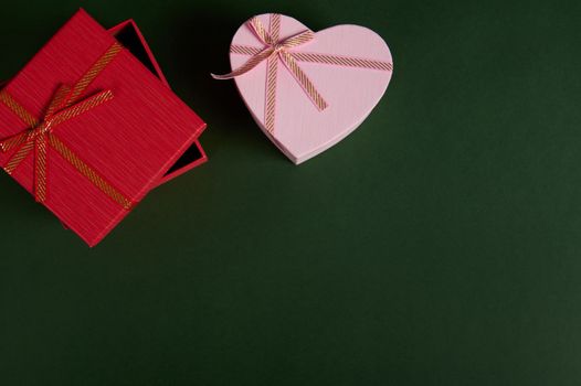 Various cute gift boxes, a red square shaped and pink heart shaped on a green background with copy advertising space. Romantic surprises and presents for Christmas, St Valentine's Day and Women's Day