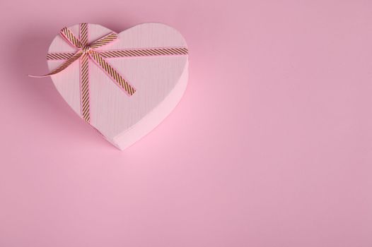A romantic present, a heart shaped pink gift box with a cute surprise for Saint Valentine's or Women's Day, in the corner of a pastel pink background with copy advertising space. February 14, March 08