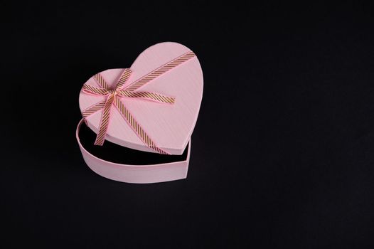 Still life. Top view composition with an open heart shaped pink gift box with tied bow, isolated on black background with copy advertising space. Romantic present for Saint Valentine's or Women's Day
