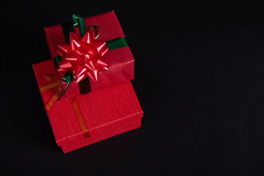 Top view of stacked red gift boxes with tied bows for Christmas, isolated on black background with copy advertising space. Christmas gift boxes, New Year Gift Boxes. Boxing Day. Present. Surprise