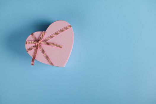 Top view Saint Valentine's day or International Women's Day heart shaped gift box, with pink ribbon bow, on pastel blue background with copy advertising space. March 8. February 14. Anniversary gift