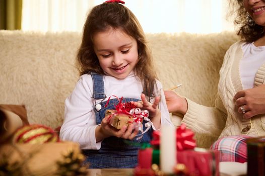 Caucasian delightful cute baby girl rejoices at a Christmas present. Enjoying winter holiday. Magical festive atmosphere at home. Boxing Day. Preparing for Xmas and New Year. Happy carefree childhood