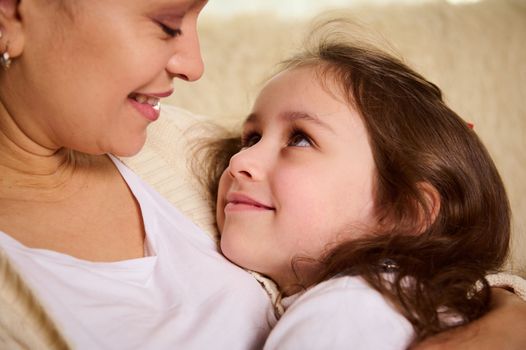 Close-up of a cute child, adorable lovely baby girl smiling cutely looking at her loving mother hugging her. Happy carefree childhood. Love Affection Tenderness. Mother's and Children's Day concept