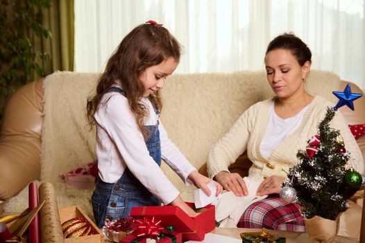 Beautiful multi-ethnic woman, loving mother and her adorable little daughter packing presents for Christmas, doing New Year preparations. Magical atmosphere of winter holidays. Xmas. December 25th