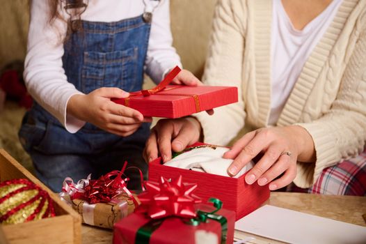 Close-up mother and daughter packing presents for Christmas or New Year, looking forward at the upcoming winter holidays. Happy family relationships. Magical festive atmosphere at cozy home interior