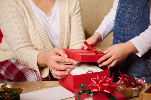 Details: hands of a woman - mom and kid - daughter packing presents in beautiful stylish red gift box. Happy magical Christmas atmosphere at home. New Year's preparations. Winter holidays atmosphere