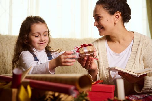 Happy family concept. Magical festive atmosphere of winter holidays. Mom and daughter pack Christmas presents, smile happily while spending time together in cozy home interior during winter holidays