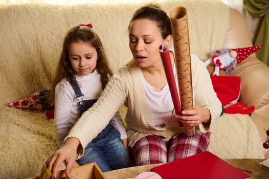 Loving mom and daughter enjoy the upcoming winter holidays, packing unwrapping Christmas New Year presents gift boxes at home together