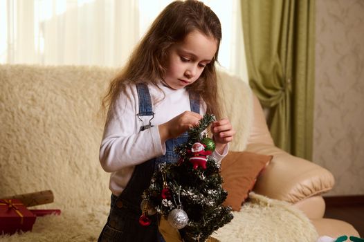 Beautiful Caucasian little girl hanging decorative balls and Christmas ornaments on a Christmas tree