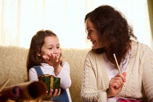 Happy multi-ethnic family of a loving mother and her beloved little daughter writing a gift list, wrapping beautiful presents for the upcoming winter holidays. Merry Christmas. New Year preparations