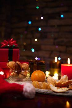 Still life with juicy tangerines, homemade delicious cookies on festive Christmas table. Blurred background with sparkling colorful garland hanging on brick wall. Celebrating New Year. Winter holidays