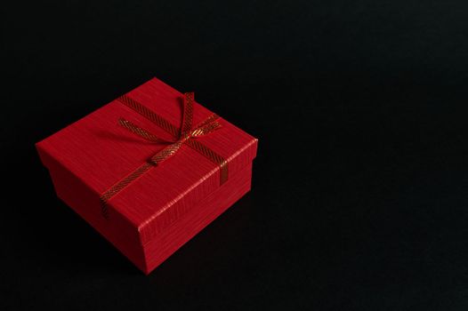 Still life red cardboard present box with a tied bow isolated on a black background with advertising copy space. Web banner. Top view of Christmas gift with surprise, packed in an elegant gift box.