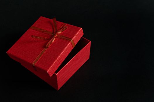 Still life red cardboard gift box with an opened lid and tied bow, isolated over black background with advertising copy space. Christmas or Valentine's Day concept. Boxing Day. Anniversary