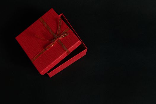 Half open elegant red cardboard gift box with a tied bow isolated on a black background with copy ad space for promotional text. Christmas gift. Valentine's Day. Women's Day. Mothers Day. Black Friday