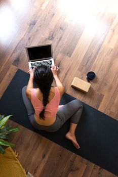 Vertical image of top view of young woman using laptop to search online yoga class. Copy space. Fitness and technology concept.
