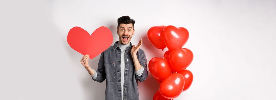 Man scream of joy and happiness, showing big red heart cutout on Valentines day, confess in love, going on romantic date and cheering, standing against white background.