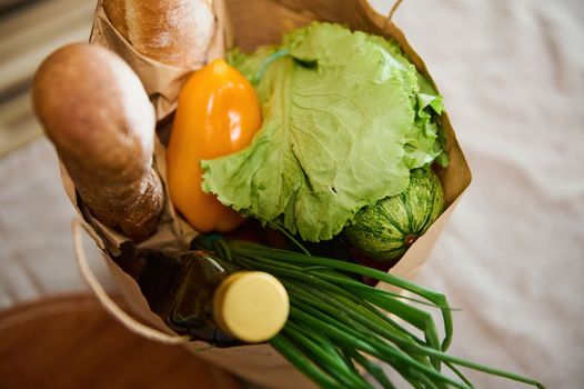 Top view eco paper shopping bag with healthy wholesome food before unpacking on a kitchen table. Healthy eating concept. Vegan food.