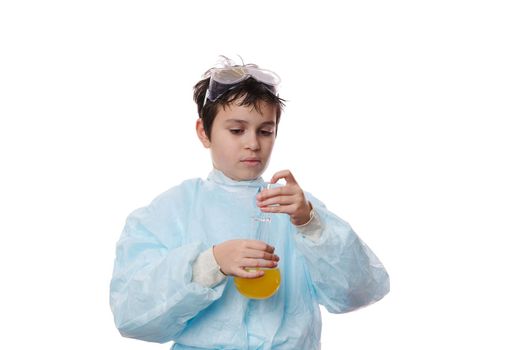 Smart teenage schoolboy in protective laboratory coat, conducts a scientific experiment in a chemistry lesson, using a glass rod, mixes reagents with chemicals in lab flask, isolated on white backdrop
