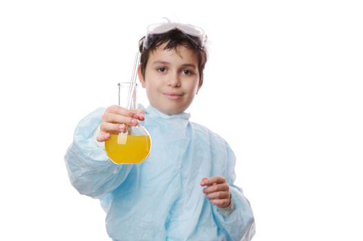 Focus on laboratory glass flask with yellow chemical solution, in the hands of a blurred smart teenage schoolboy, scientist chemist in lab coat, isolated over white background. Learning Chemistry