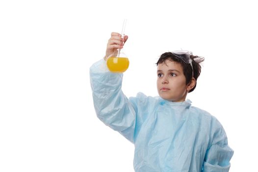 Handsome Caucasian schoolboy, a scientist chemist in a white lab coat, holding glass laboratory flasks with chemicals, watching the reaction taking place between liquid and reagents. Chemistry class.
