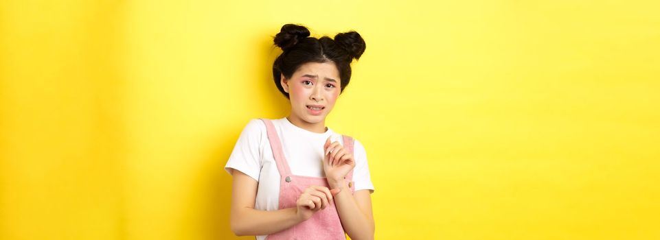 Stay away. Reluctant timid asian girl step back, raising hands to block something disgusting, grimacing displeased, say no, rejecting with aversion, yellow background.