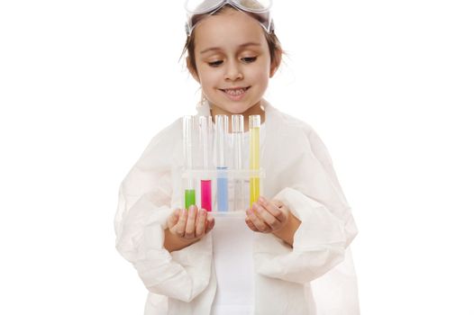 Selective focus on test tubes with colorful reagents and chemicals on tripod in the hands of a blurred child, little girl, young chemist scientist in lab coat, isolated on white background. Copy space