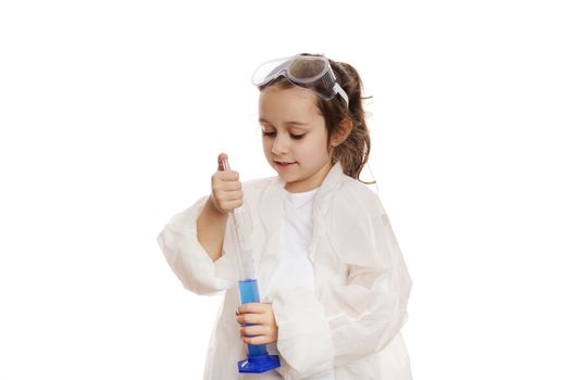 Smart little girl, student chemist-scientist in lab coat, dripping few drops of reagent from graduated pipette into a measuring cylinder with chemical solution, at a chemistry lesson. White background