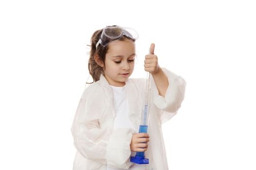Smart primary school student, little girl in lab coat, filling the glass laboratory graduated pipette with a blue liquid chemical solution from a measuring cylinder. Kids learning chemistry. Education
