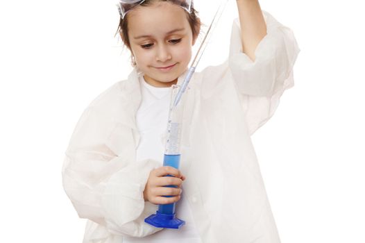 Close-up portrait of a little girl, young chemist scientist, filling the glass laboratory graduated pipette with a blue chemical solution from a measuring cylinder, isolated over white background