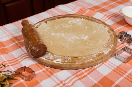 Still life with floured rolled out gingerbread dough and rolling pin on a wooden board. Cookies cutters on the red plaid tablecloth