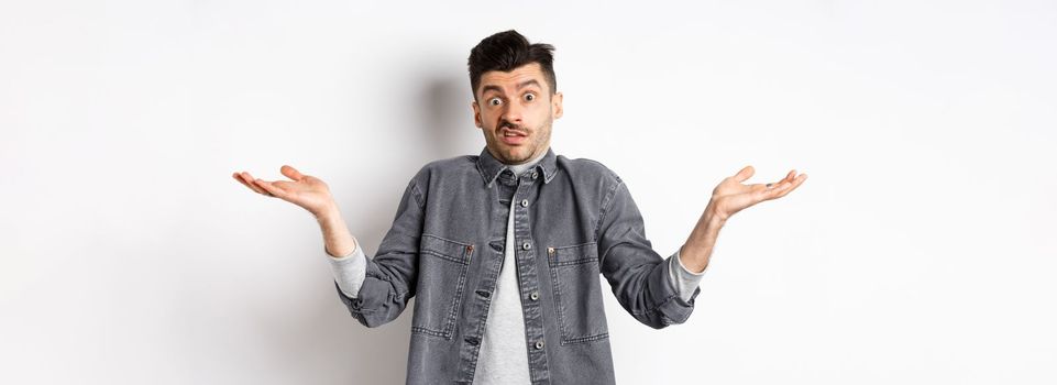 I dont know. Clueless young man shrugging and looking confused, have nothing to say, standing unaware on white background.