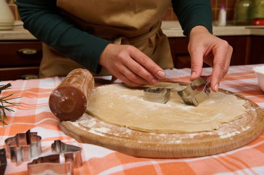 Details: hands of a chef confectioner putting metal cookies cutters on a rolled out gingerbread dough, preparing delicious homemade pastries for Christmas holidays in the kitchen at home