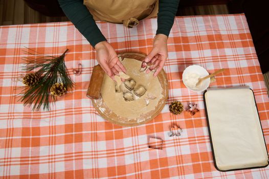 Directly above housewife's hands holding an angel wings shaped mold from gingerbread dough. Making cookies for Christmas. Chef confectioner baking homemade delicious festive cookies in the kitchen