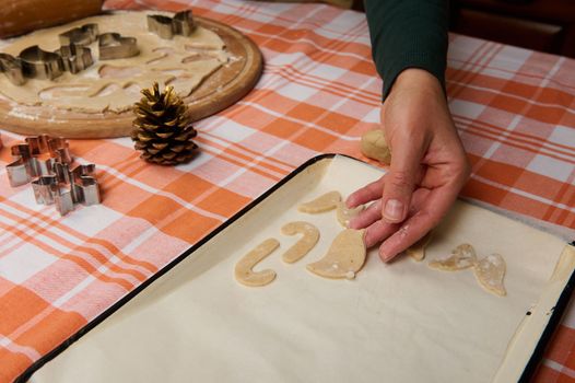 Detail: hand of a chef confectioner putting candy cane shaped gingerbread dough on the parchment before baking cookies in the oven. Preparing homemade delicious festive pastries for Christmas holidays