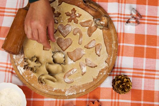 Directly above a chef confectioner's hand taking cookie cutters out of rolled gingerbread dough, preparing festive pastries for Christmas holidays. Housewife baking festive cookies in the home kitchen