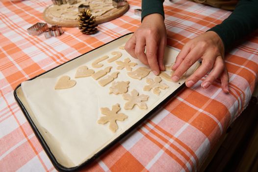 Details: Hands of woman confectioner laying out the cut out shapes from gingerbread dough, on a baking sheet, for placing in the oven