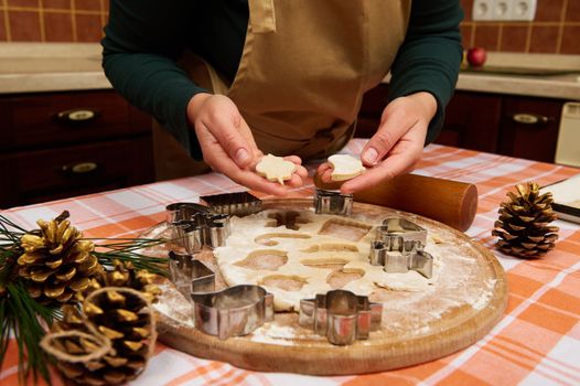 Cropped view of a housewife, wearing a green shirt and a beige chef's apron, showing to the camera Christmas cookies, cut out of gingerbread dough. Woman confectioner making festive pastries