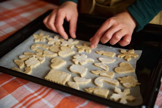 A woman chef confectioner puts gingerbread cookies on the baking paper. Homemade cookies cut with various molds - candy canes, angel wings, heart, snowflake, candle, bird, before baking in the oven