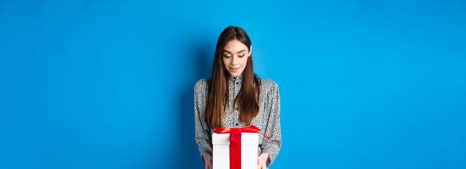 Valentines day. Surprised caucasian woman gasping amazed and looking at romantic gift, standing on blue background.