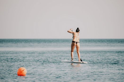 Sea woman sup. Silhouette of happy middle aged woman in rainbow bikini, surfing on SUP board, confident paddling through water surface. Idyllic sunset. Active lifestyle at sea or river