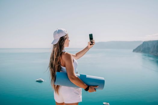 Young woman with black hair, fitness instructor in pink sports leggings and tops, doing pilates on yoga mat with magic pilates ring by the sea on the beach. Female fitness daily yoga concept